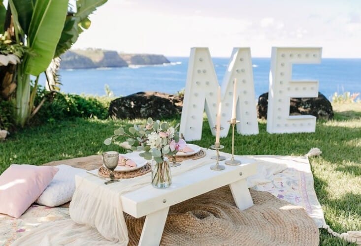 A picnic table with "marry me" marquis signage, the ocean, and Maui's North Shore in the background.